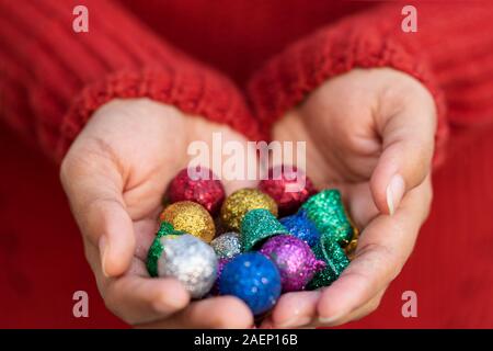 Girl holding colorful christmas balls in her hand and wearing red sweater. Background concept for christmas card, greeting card, wallpaper. Stock Photo