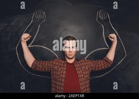 Young man against the background of depicted muscles on chalkboard Stock Photo