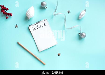 Christmas Wish List written on paper with cup of tea, pencil and Christmas festive decor, flat lay on blue pastel background. New Year's wishing and p Stock Photo