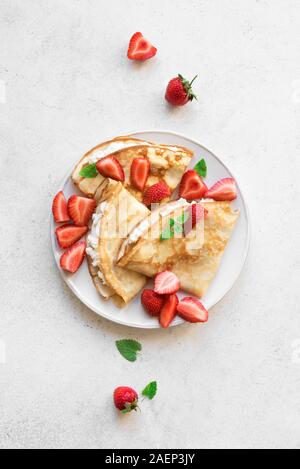 Crepes with ricotta cheese and fresh strawberries on white background, top view, copy space. Delicious crepes, thin pancakes. Stock Photo