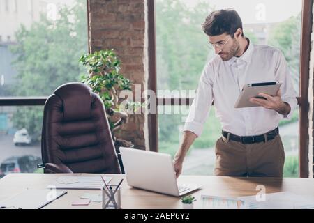 Portrait of serious concentrated middle eastern chief man leader economist working on computer hold tablet send emails to startup partners stand near Stock Photo