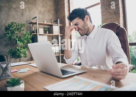 Profile side photo of tired middle eastern entrepreneur man have much work on laptop try concentrate touch his nose hold glasses sit desk in loft Stock Photo