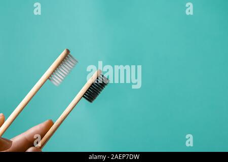 Two wooden bamboo eco friendly toothbrushes in male and female hands on aquamarine background. Dental care, family and zero waste concept. Flat lay, t Stock Photo
