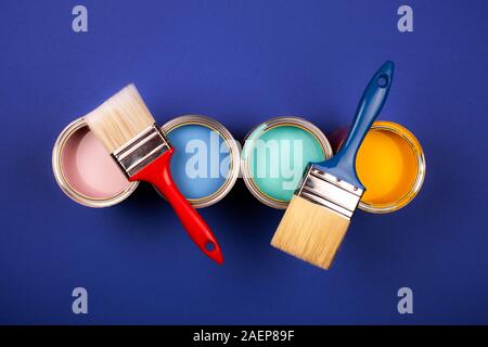 Four open cans of paint with brushes on blue background. Yellow, blue, pink, turquoise colors of paint. Top view. Stock Photo