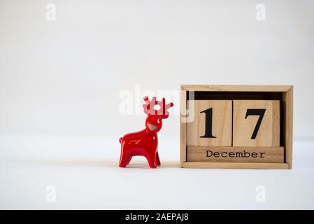 Cube wooden calendar showing date on 17th December with ceramic reindeer figurine over white background. Advent calendar, Christmas background Stock Photo