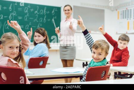 Students in class raising hands to answer a question Stock Photo
