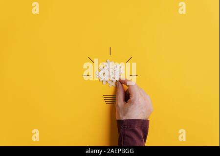 Male hand making a light bulb with puzzle pieces and marker in a conceptual image of creativity and idea. Over yellow background with copy space. Stock Photo