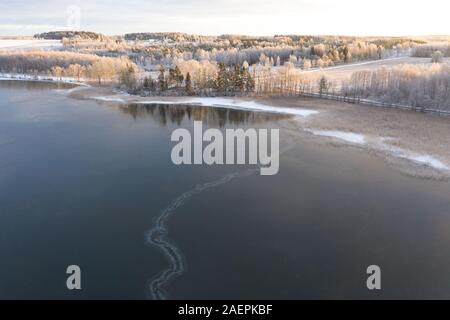 Aerial drone view of a lake coast starting to freeze over in winter sunrise light. Tartu, Estonia. Stock Photo