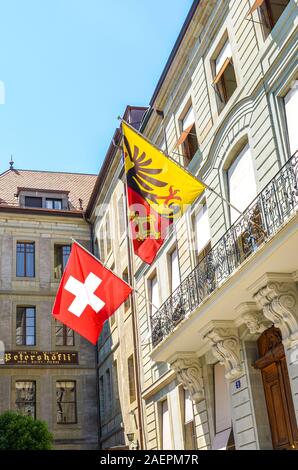 Geneva, Switzerland - July 19, 2019: Old town buildings in the city center with waving Swiss flag and the flag of Geneva. Facades of the historic houses. Vertical photo. Stock Photo