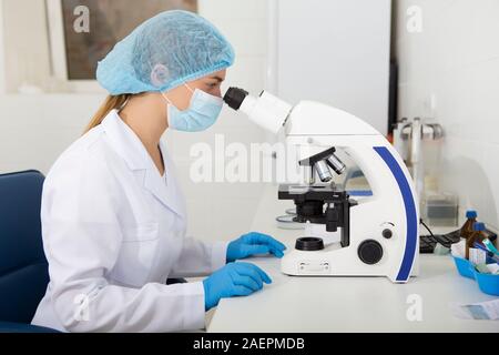 Young woman in medical clothes working with microscope Stock Photo