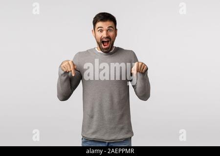 Hey see this, check it out. Impressed and happy, fascinated attractive bearded boyfriend invite for awesome christmas party, pointing down looking you Stock Photo