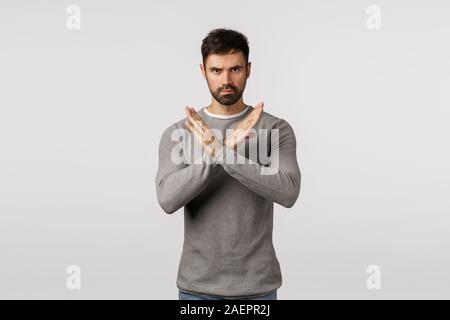 No, never accept it. Serious, confident bearded man in grey sweater, making cross stop gesture, restrict partner doing bad action, give negative reply Stock Photo