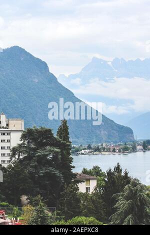 Famous city Montreux in Switzerland on a foggy day. Buildings by beautiful Lake Geneva, Swiss Alps in the background. Popular tourist destination, Swiss Riviera. Vertical picture. Stock Photo