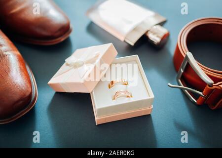 Groom's wedding day preparation accessories. Brown leather shoes, belt, perfume, golden rings in box on grey background. Male fashion Stock Photo