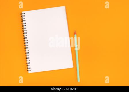 Empty notebook and pencil on orange background, top view. Stock Photo