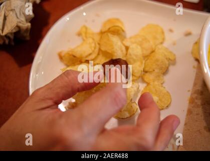 Fingers about to remove a burned potato chip from plate Stock Photo