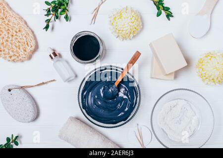 Homemade black clay face mask. Cosmetic products and accessories for skin care, top view on white table. Stock Photo