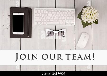 Wireless slim keyboard and mouse, smartphone, notepad, glasses, flower and text Join our team on white wooden background Stock Photo