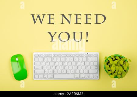 Wireless slim white keyboard and green mouse and text We need you on yellow paper background Stock Photo