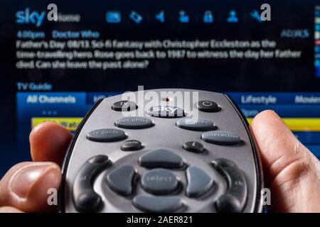 A Man holding a Sky TV remote control, pointing at the TV Stock Photo