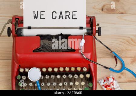 Prescription medicine or medical diagnosis - doctor workplace with blue stethoscope, pills, red typewriter with text We care on wooden table Stock Photo