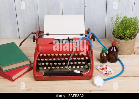 Prescription medicine or medical diagnosis - doctor workplace with blue stethoscope, pills, red typewriter with blank paper on wooden table Stock Photo