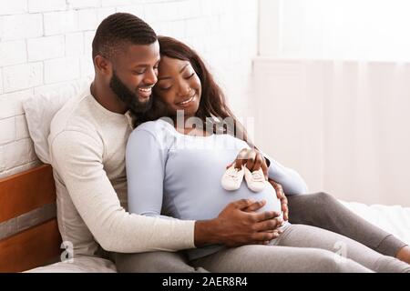 Pregnant couple putting future baby little boots on tummy Stock Photo