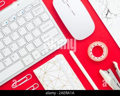 Flay lay, Top view of Feminine desk workspace frame, notebook, keyboard, mouse, pen, pencil, paper clips and stapler on red Christmas background. Blog Stock Photo