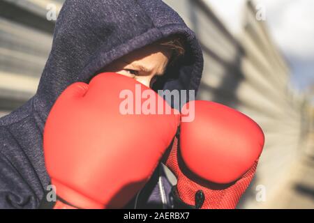 Portrait of handsome young male with boxing gloves ahead the face. Boy ready for a boxe workout defending the head with hands. Boxer ready to throw pu Stock Photo