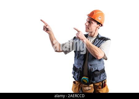 The builder points to the left. Offers with index fingers. In work clothes and hard hat. Stock Photo