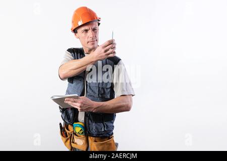 A builder in a helmet makes visual measurement with a marking pencil. Stock Photo