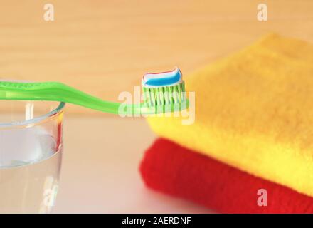 close-up of a green toothbrush with toothpaste on a glass of water, colorful towels in the background Stock Photo