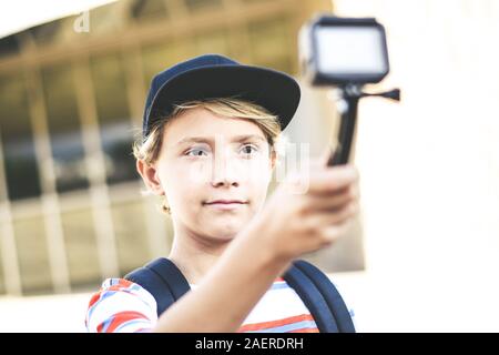 Closeup view of a teen with hat taking selfie with action cam Young blogger making video for social story with GoPro camera Student having fun Stock Photo