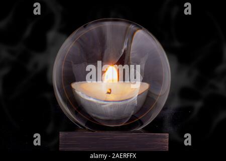 A crystal ball with a candle reflected in it against a black smoky background. Stock Photo