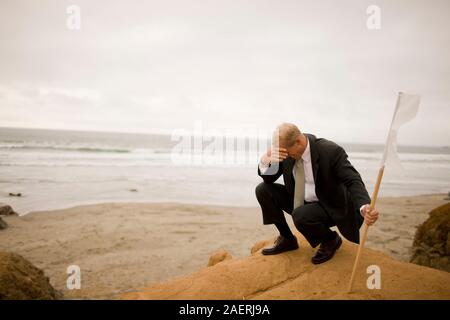 Upset businessman holding white flag at beach Stock Photo