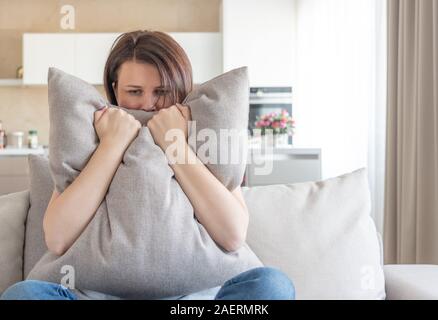 Sad depressed woman at home, she is sitting on the couch and hugging a pillow, loneliness and sadness concept Stock Photo