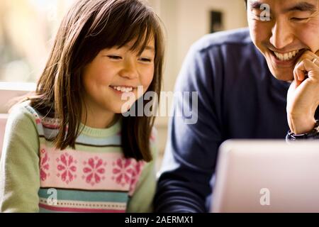 Father and daughter smile while working on a laptop together. Stock Photo