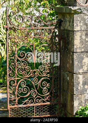 Old, ornate, rusty metal garden gate with wrought iron scroll decoration and stone gatepost, Colonsay House Gardens, Colonsay, Scotland, UK Stock Photo