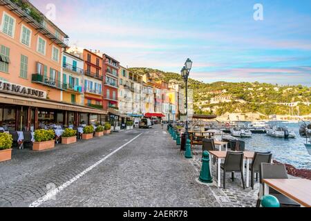 Tourists walk a cobbled street in front of a row of colorful apartments and cafes in Villefranche Sur Mer, France, on the Mediterranean Riviera Stock Photo