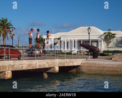 Three kids preparing to dive from the Ordnance Island bridge in St. George's, Bermuda. somewhat dangerous, but exhilarating. Stock Photo