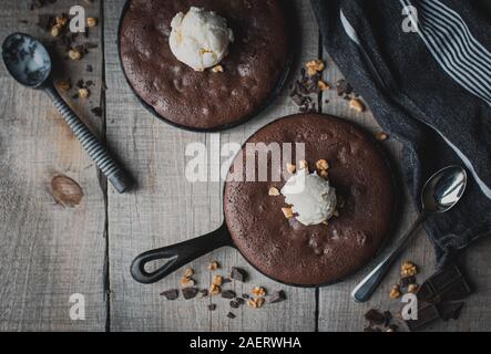 Top view of brownies with ice cream and nuts in cast iron skillets. Stock Photo