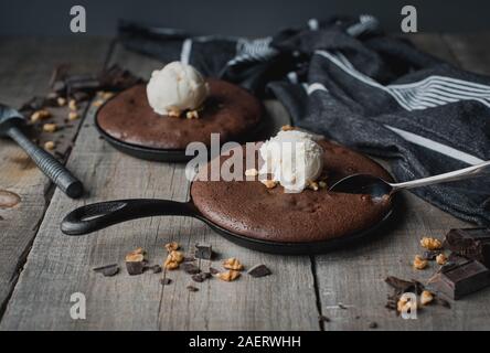 Brownies with ice cream and nuts in cast iron skillets on wooden table Stock Photo