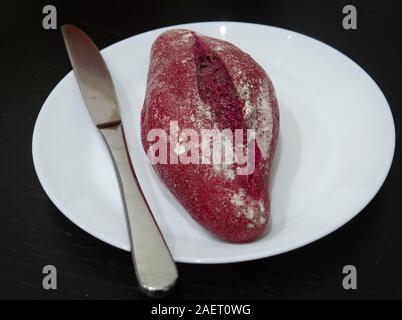 Red beet bread bun with a knife on a white plate Stock Photo