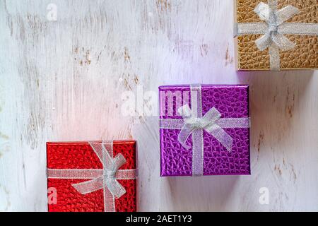 Flat lay. Three gift boxes with bows on a white surface painted with a brush. Red, purple and gold boxes. Copy space. Stock Photo