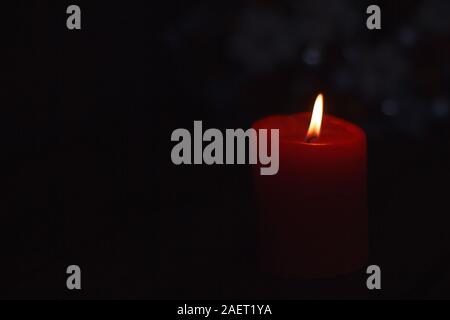 A single burning red candle isolated against black backdrop Stock Photo
