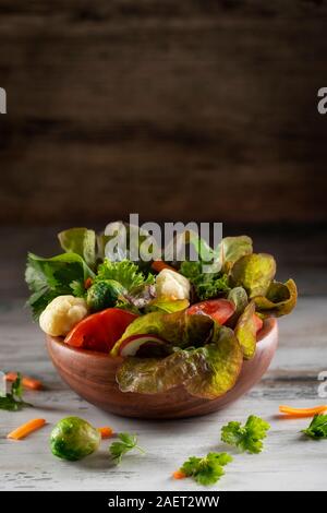 Fresh mixed green salad with  tomatoes,  brussels sprout, broccoli cauliflower, lettuce and spinach in wooden bowl on a brown background. Mock up Stock Photo