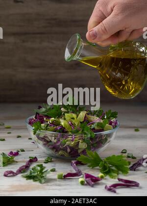 Salad of red cabbage in a glass salad bowls on a wooden background. A hand is holding a bottle of olive oil that is trickling into a salad bowl. Stock Photo