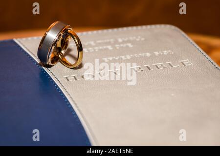 A pair of wedding bands standing on top of a Holy Bible cover.