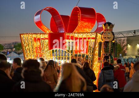 Crowds of people around a large Christmas present wrapped in a red ribbon flanked by a toy nutcracker soldier at Torrejon de Ardoz Christmas Fair Stock Photo