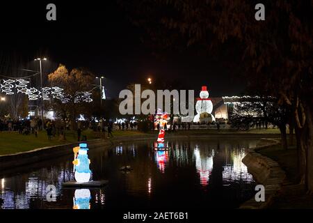 An inflated illuminated Santa Claus and Snowman in the middle of a small lake dominated by a much larger snowman with a red hat Stock Photo